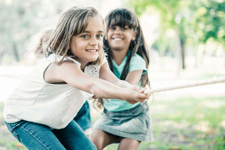 Team of happy kids pulling rope, playing tug-of-war, enjoying outdoor activities. Group of children having fun in park. Childhood or teamwork conceptの写真素材