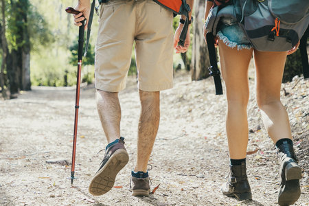Back view of couple hiking together on road. Unrecognizable man and woman walking on nature. Legs of...
