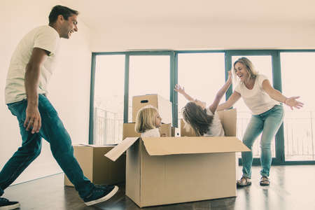 Active girls bursting out from carton box. Parents and two daughters having fun while unpacking...