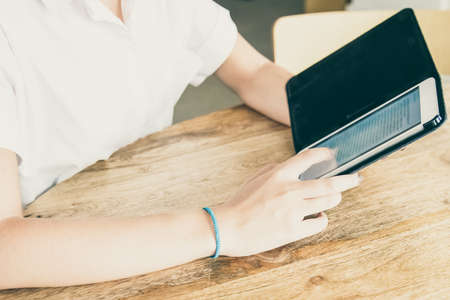 Young woman wearing white shirt, using tablet in open flip case, reading text on screen while sitting at table. Cropped shot. Digital communication conceptの写真素材