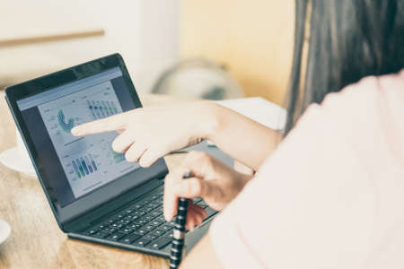Analyst explaining diagrams to customer. Business women meeting at table over cup of coffee and analyzing charts on laptop display. Cropped shot of screen and hands. Consulting or analysis conceptの写真素材