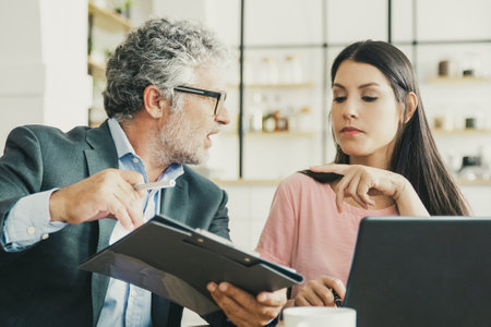 Serious mature legal expert reading, analyzing and explaining document to female customer. Man and woman sitting at table and discussing papers. Expertise and paperwork conceptの写真素材