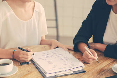 Young female colleagues meeting and discussing business plan, writing strategy scheme on paper, making draft. Cropped shot. Planning conceptの写真素材