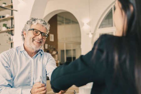 Happy mature businessman in glasses shaking hands with female partner at meeting in co-working space. Partnership or cooperation conceptの写真素材