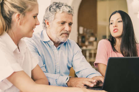 Business team of three sitting at laptop, watching and discussing content. Mature man and young...
