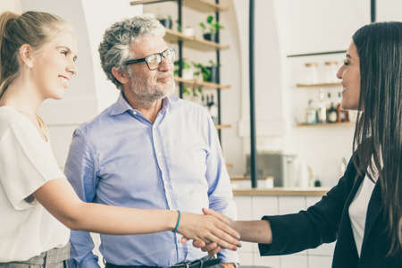 Happy confident female manager meeting with customers and shaking hands. Man and women in co-working space. Side view. Partnership or business meeting conceptの写真素材