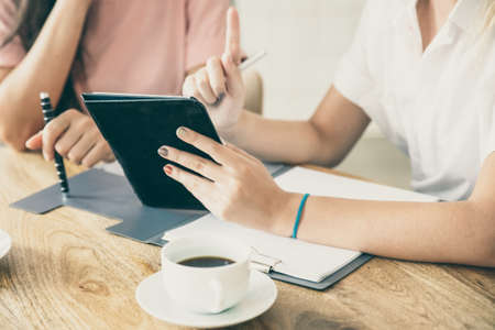 Business ladies meeting at table, watching presentation on tablet, discussing project or deal. Cropped shot of table and hands. Consulting or cooperation conceptの写真素材