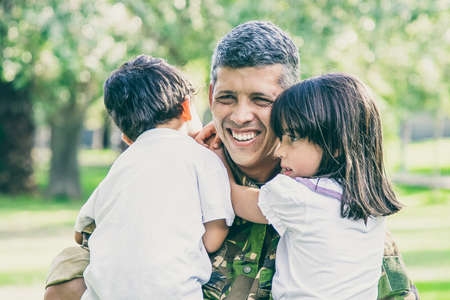 Happy military father meeting with children after military mission trip, holding kids in arms and...