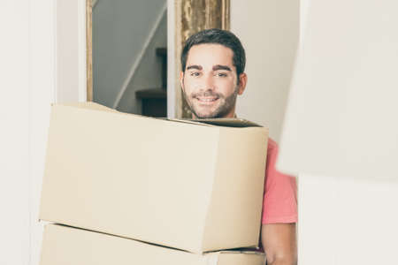 Happy man moving into new apartment, walking through doorway and carrying boxes. Side view. Loader occupation or delivery service conceptの写真素材