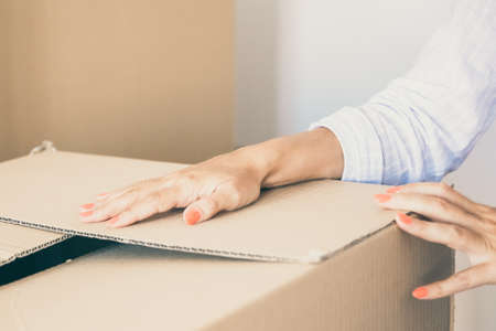 Woman packing things for moving. Closeup of female arms on carton box. Cropped shot. Relocation or new home conceptの写真素材