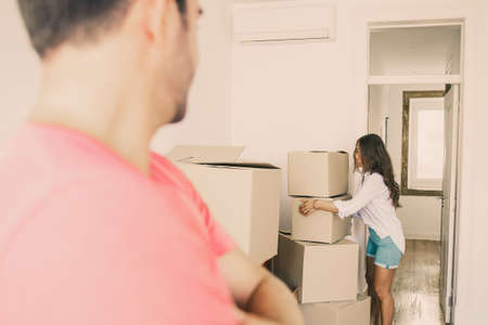 Man in pink t-shirt holding key from his new apartment, standing with arms folded and watching his...