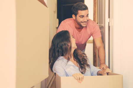Happy excited family couple having fun while moving into new apartment. Cheerful young man dragging box with his girlfriend inside. New home conceptの写真素材