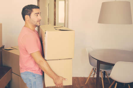 Focused man carrying carton boxes into new apartment, moving into new flat. Side view. Loader occupation or delivery service conceptの写真素材