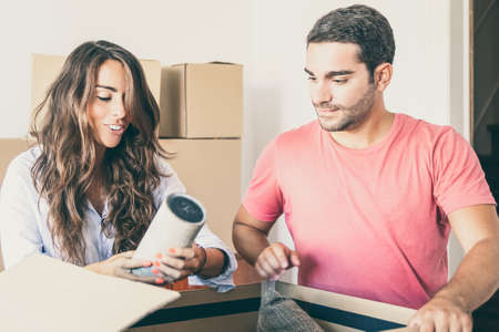 Cheerful young man and woman moving and unpacking things, opening carton box and getting out object. Relocation or new home conceptの写真素材