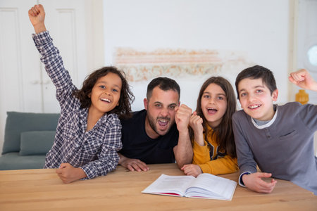 Bearded dad and children happy that they completing tasks. Caucasian father, daughter and sons rising their hands up, sitting at table and smiling. Family time, education conceptの写真素材