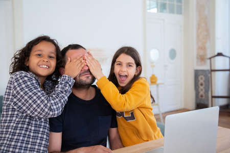 Kids having fun with father while learning at home. Smiling curly-haired boy and girl sitting at...
