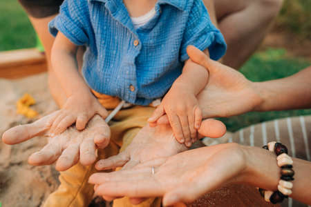Close-up of child and woman playing with sand in sandpit. Hands of toddler girl and her mother in...