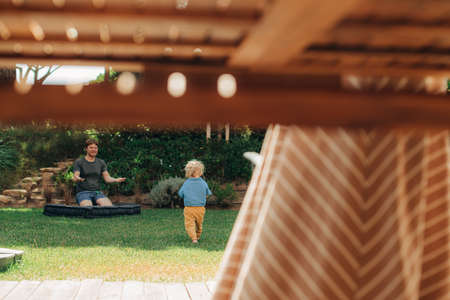 Little girl running to her father on backyard, her mother standing at table outdoors. Happy man...