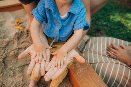Close-up of male and childish hands in sand. Father and toddler daughter sitting in sandpit showing dirty palms. Fatherhood and family leisure conceptの写真素材