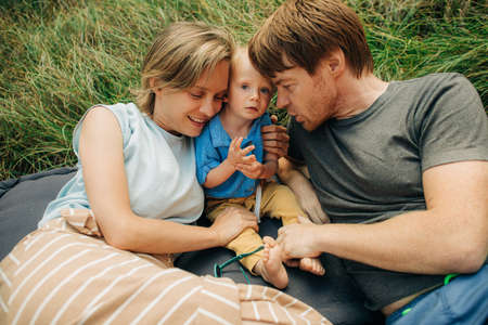 Portrait of loving parents resting with child. Smiling man and woman lying on mattress embracing toddler daughter. Family vacation conceptの写真素材