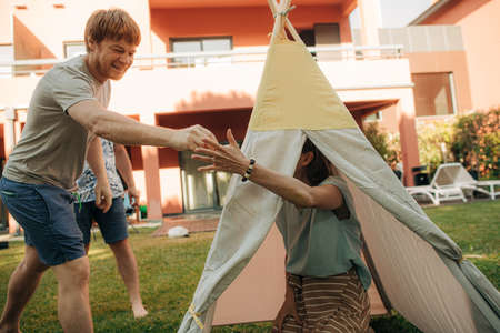 Happy family resting in front yard at their house. Woman sitting in wigwam tent, her husband...