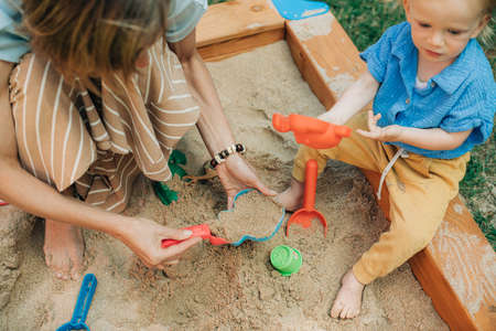 Mother and child playing together in sandpit. Woman playing with little daughter on playground outdoors. Childhood and parenthood conceptの写真素材
