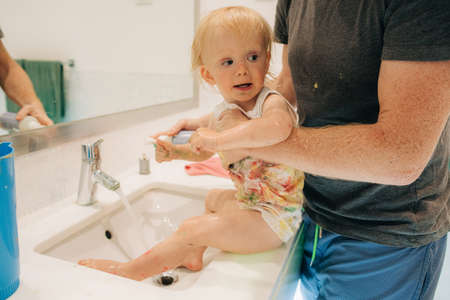 Father washing little girl in bathroom sink. Portrait of messy baby girl in fathers hands. Childcare...