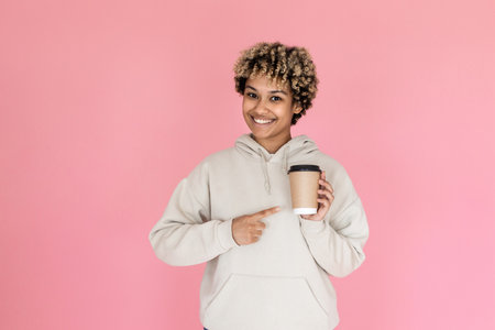 Lovely African American woman drinking coffee in studio. Female model with curly hair holding disposable cup with drink. Portrait, beverage, studio shot conceptの写真素材