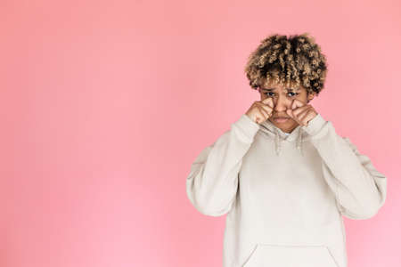Unhappy African American woman in studio. Female model in hoodie with curly hair looking at camera,...