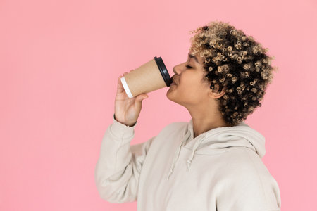 Tranquil African American woman drinking coffee in studio. Female model with curly hair holding disposable cup with drink. Portrait, beverage, studio shot conceptの写真素材