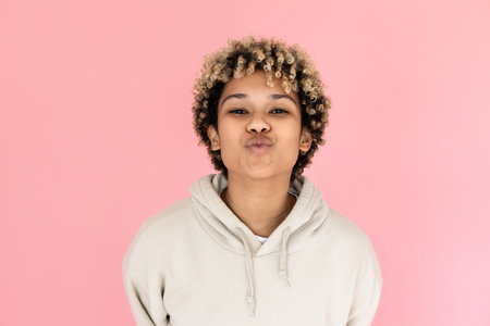Beautiful African American woman blowing kiss. Female model with curly hair kissing camera in studio. Portrait, studio shot conceptの写真素材