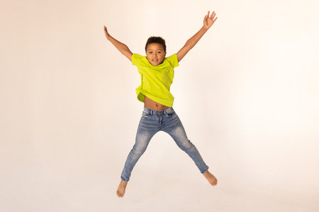 Portrait of happy preteen boy jumping against white background. Excited mixed race child wearing green T-shirt and jeans having fun. Happiness conceptの写真素材