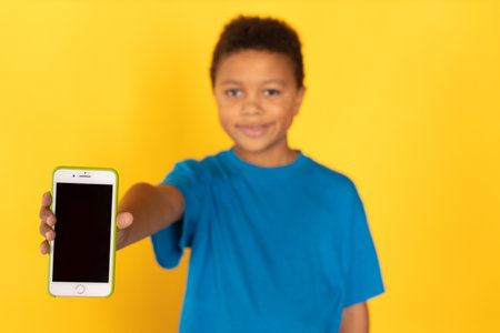 Happy preteen boy wearing blue T-shirt showing smartphone. Portrait of mixed race child looking at...