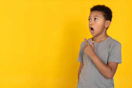 Portrait of surprised preteen boy pointing at something. Mixed race child wearing gray T-shirt looking upwards and showing something. Astonishment conceptの写真素材