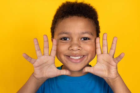 Close-up of funny preteen boy wearing blue T-shirt making face. Happy mixed race child showing palms against yellow background. Fun conceptの写真素材