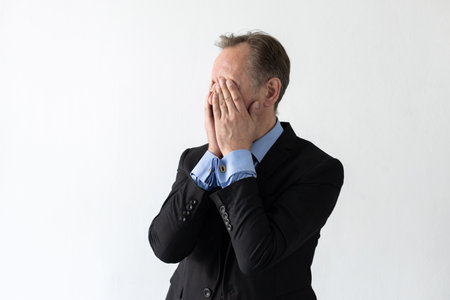 Portrait of upset mature businessman covering face with hands. Senior Caucasian manager wearing three piece suit having problem or getting stressed against white background. Stress or problem conceptの写真素材
