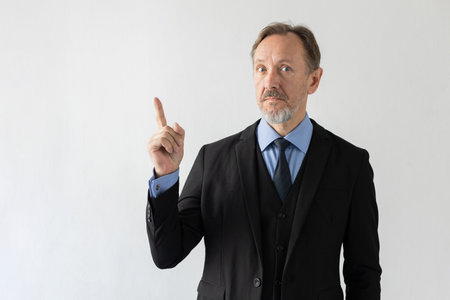 Portrait of surprised mature businessman getting solution. Senior Caucasian man wearing three piece suit looking at camera showing index finger. Idea, solution and business strategy conceptの写真素材