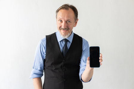 Portrait of positive mature businessman showing mobile phone against white background. Senior...