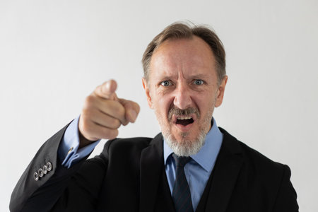Portrait of furious mature businessman blaming someone and pointing at camera. Angry senior...