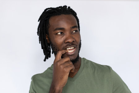 Closeup of thoughtful African American man biting nail. Unsure young male model with braided dark hair in green T-shirt looking away at ads, struggling to decide. Advertisement, choice concept.の写真素材