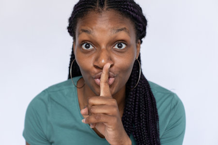Excited woman holding finger at lips. Young female model in turquoise T-shirt making hush gesture...