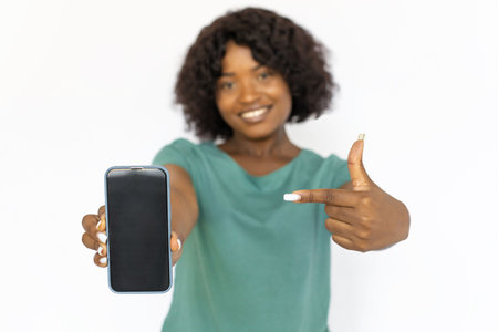 Pretty young woman pointing at smartphone. Smiling African American female model in blue T-shirt...