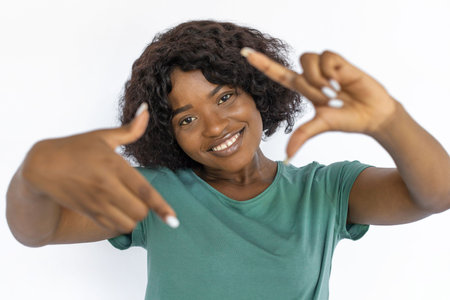 Cute young woman making photo frame gesture. Cheerful African American female model with short black...