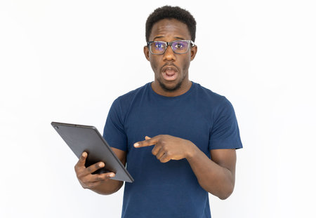Surprised man pointing at tablet. Young African American male model holding tablet, looking at...