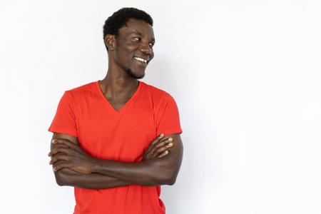 Portrait of pleased African American man looking at ad. Happy young male model with short dark hair in red T-shirt looking away with folded arms, smiling. Advertisement conceptの写真素材