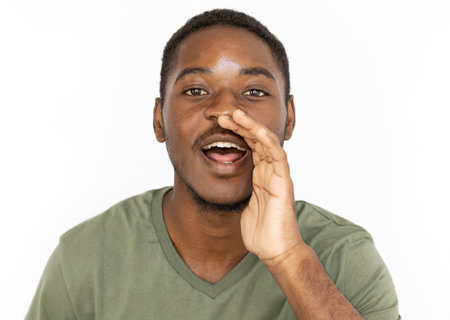 Whispering young man holding hand near mouth. Male African American model in green T-shirt holding...
