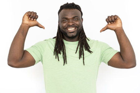 Happy African American man pointing thumbs at himself. Smiling man with dreadlocks standing against white background, being proud of himself. Self-assurance, confidence conceptの写真素材
