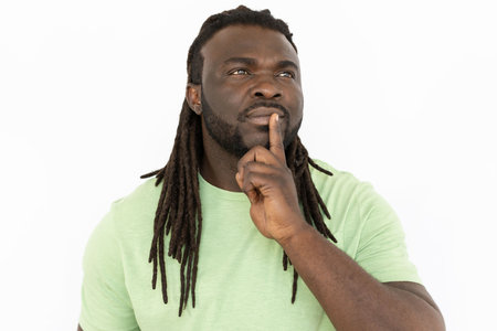 Thoughtful Black man looking up and thinking. Pensive man standing against white background, considering ideas or dreaming with his finger on mouth, feeling inspired. Planning, contemplation conceptの写真素材