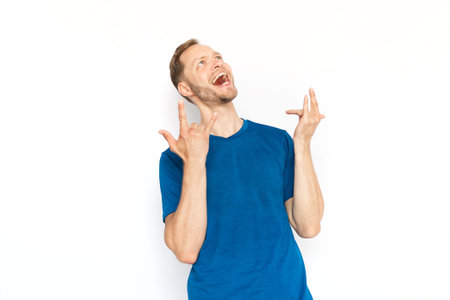 Excited man showing rock signs and rejoicing in victory.Bearded man with fair hair laughing with open mouth,receiving good news while standing on white background.Happiness, success,excitement conceptの写真素材