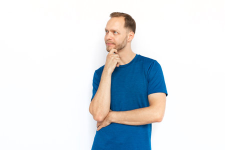 Thoughtful man touching his chin with hand and thinking. White man in T-shirt looking up, posing for camera, dreaming or considering ideas. Imagination, wonder, inspiration conceptの写真素材